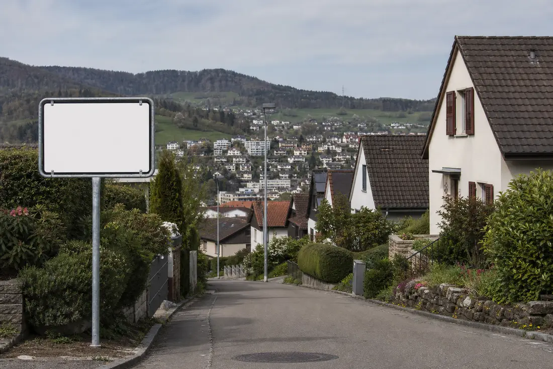Ortstafel einer Zürcher Gemeinde vor wohnlicher Agglomerationskulisse